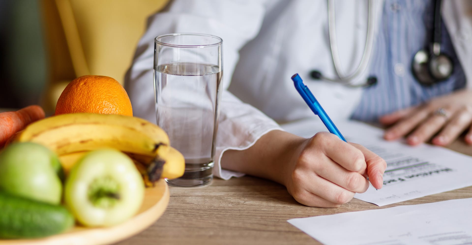A close-up of a health care provider filling out paperwork in front of a glass of water and plate of fruit