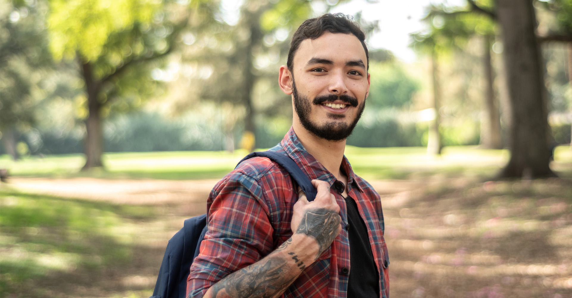 Man wearing a plaid shirt holding a backpack and smiling